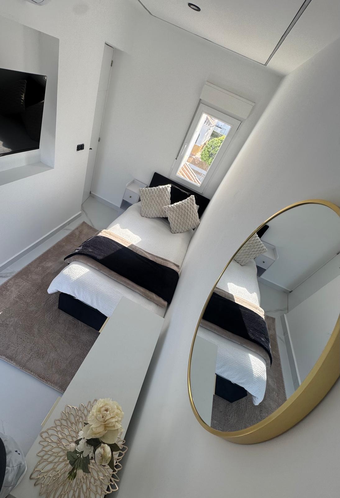Overhead view of the third bedroom with round gold mirror, styled bed and morning sunlight